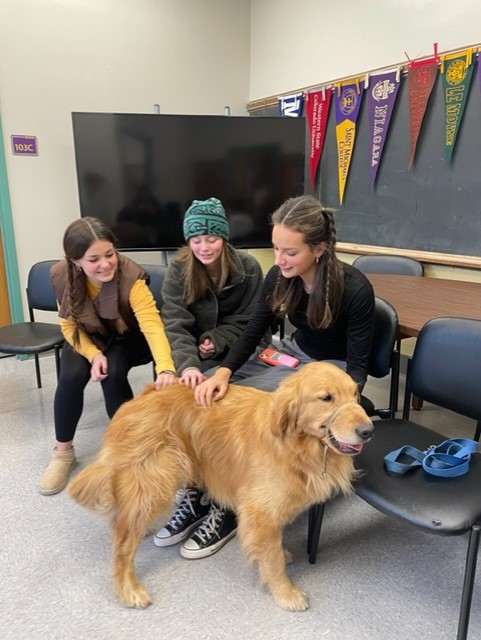 Delilah Tumolo, Ella Brick, and June Nathan (from left to right) are petting Scout, RHSs therapy dog.