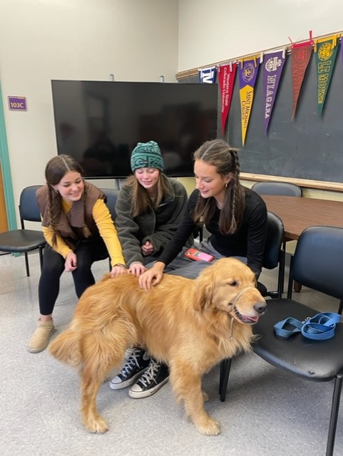 Delilah Tumolo, Ella Brick, and June Nathan (from left to right) are petting Scout, RHS's therapy dog.