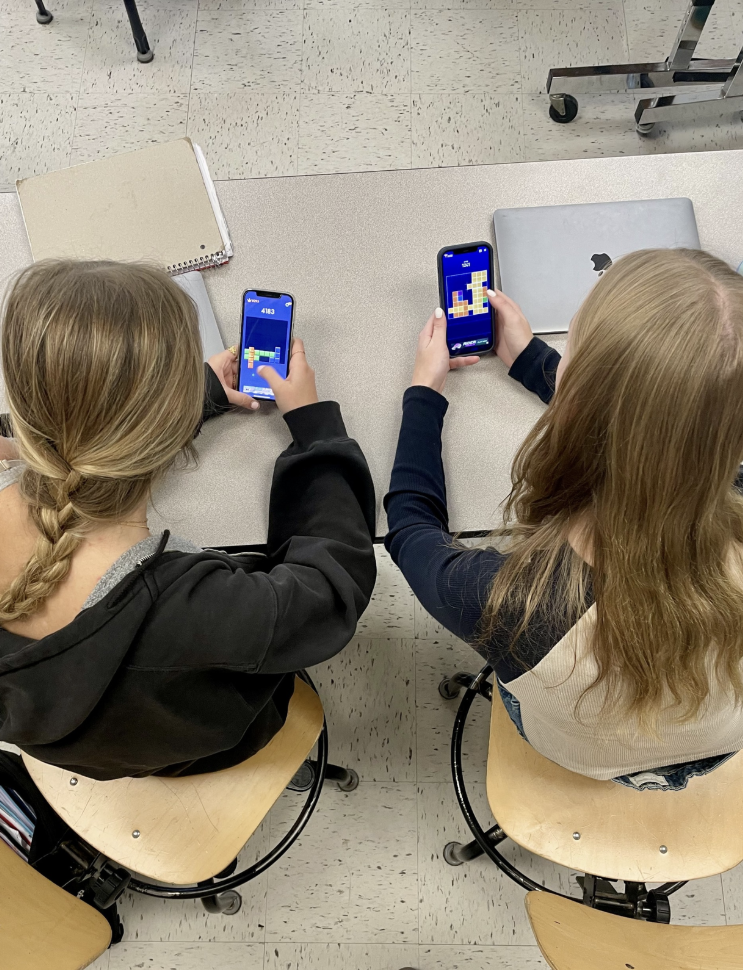 Two students playing phone games in a classroom during Community Lunch